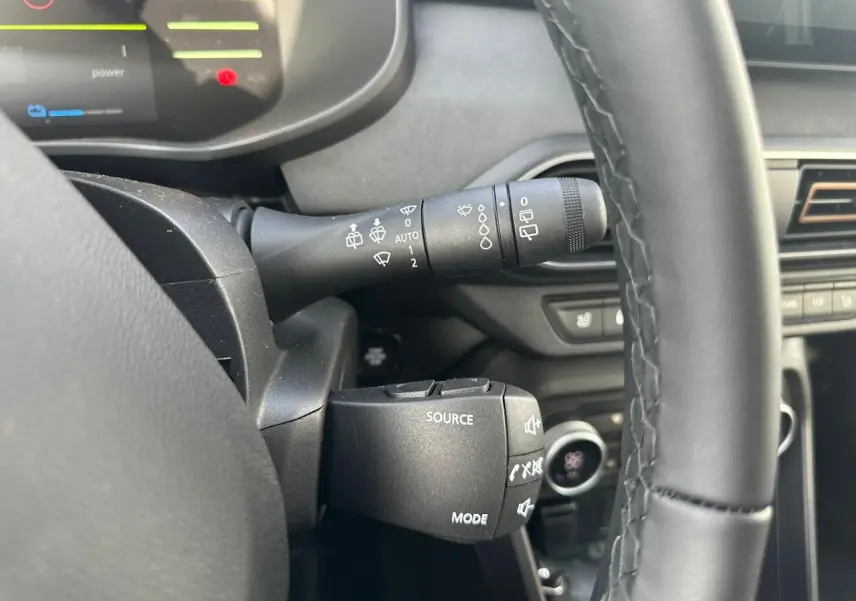 Gros plan sur la commande au volant et le commodo d'essuie-glace du DACIA JOGGER kaki, intérieur noir et détails fonctionnels visibles.