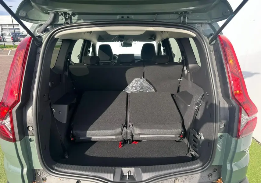 Coffre ouvert vu de l'arrière d'un Dacia Jogger kaki lichen, banquette arrière partiellement rabattue et feux arrière visibles.