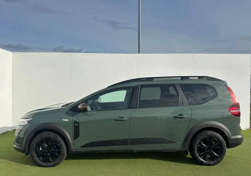 Profil droit du Dacia Jogger 2025 kaki lichen métallisé avec jantes noires et barres de toit modulaires.