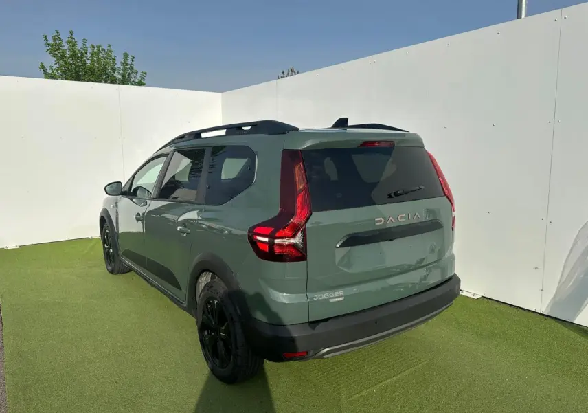 Vue 3/4 arrière droite du Dacia Jogger 2025 hybride en kaki lichen avec barres de toit et jantes noires.