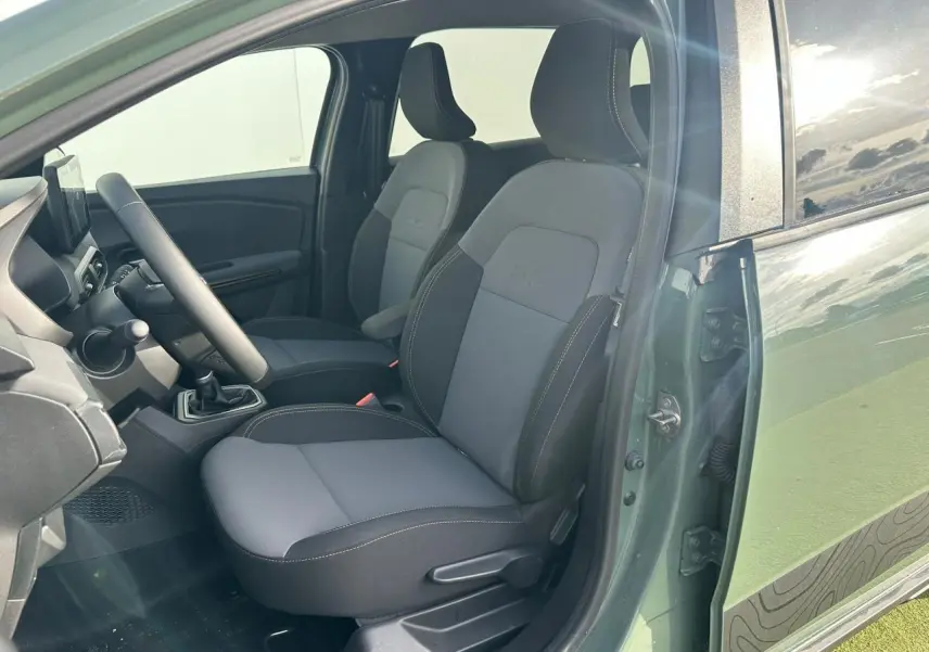 Vue intérieure côté conducteur du Dacia Jogger kaki lichen, mettant en valeur les sièges avant gris et noirs avec surpiqûres contrastées.