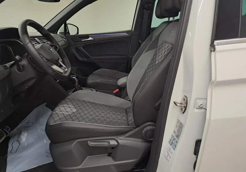 Vue intérieure côté conducteur du Volkswagen Tiguan blanc pur 2023, sièges sport R-Line en tissu et cuir gris.