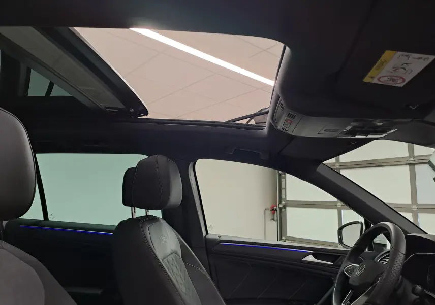 Vue intérieure du Volkswagen Tiguan blanc pur 2023, toit ouvrant panoramique et éclairage d'ambiance bleu sur les portières.