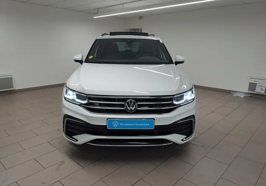 Vue frontale d'un Volkswagen Tiguan blanc pur 2023 avec phares LED allumés et calandre R-Line dans un showroom.