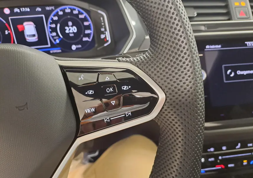 Gros plan sur le volant perforé côté gauche du Volkswagen Tiguan blanc avec commandes tactiles et tableau de bord digital.