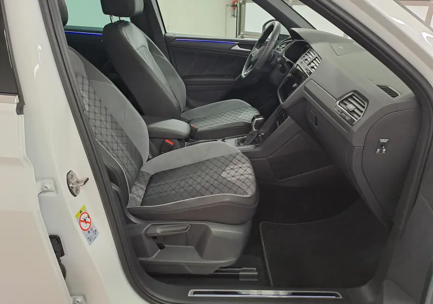 Vue intérieure côté conducteur du Volkswagen Tiguan blanc pur 2023, sièges sport gris à motifs et tableau de bord noir.