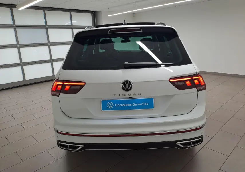 Vue arrière d'un Volkswagen Tiguan blanc pur 2023 avec feux LED allumés et double sortie d'échappement intégrée.