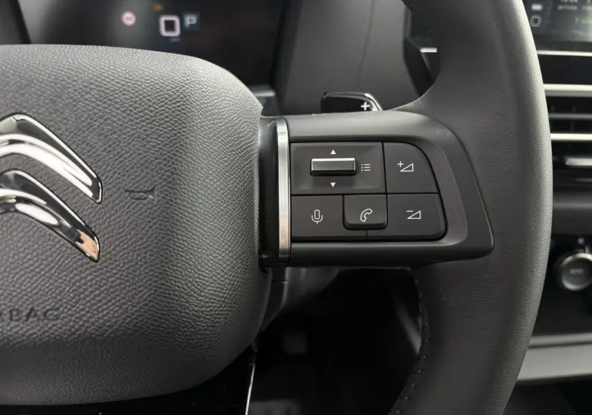 Gros plan sur le volant cuir noir de la Citroën C4 2024 avec commandes audio et logo chromé visible.