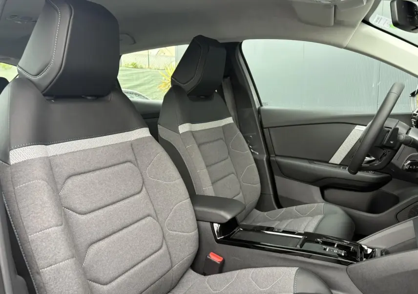 Vue intérieure côté conducteur de la Citroën C4 2024, sièges tissu gris avec accoudoir central noir brillant.