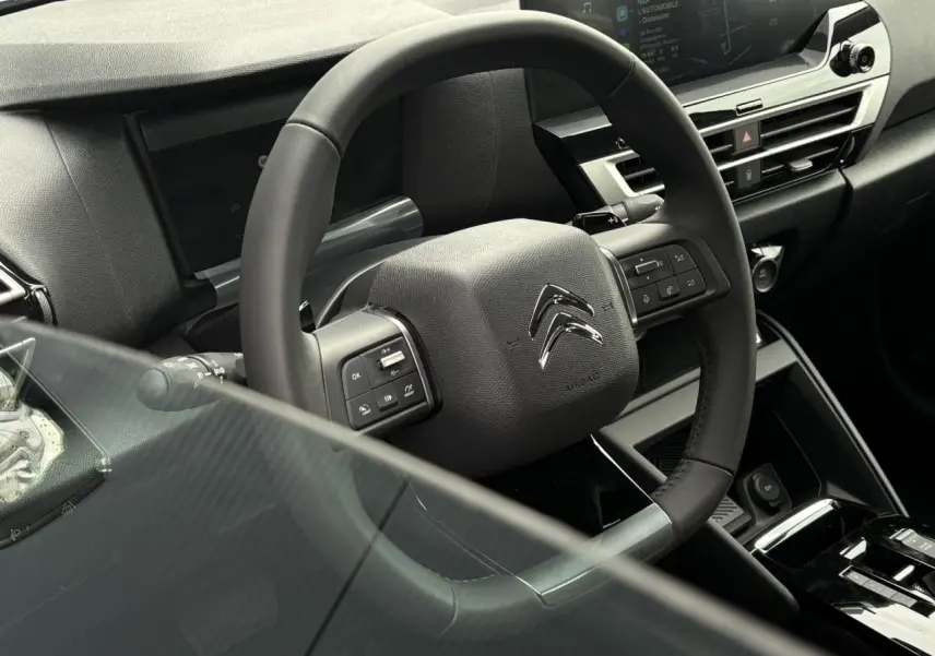 Vue rapprochée du volant cuir de la Citroën C4 2024 avec commandes intégrées et tableau de bord numérique.
