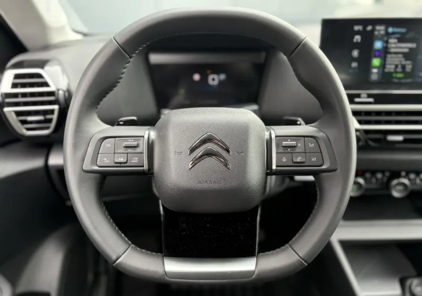 Vue rapprochée du volant en cuir noir de la Citroën C4 2024 avec commandes intégrées et tableau de bord numérique.