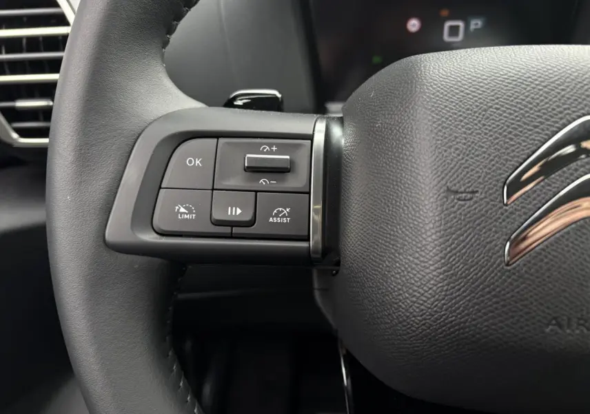 Gros plan sur la partie gauche du volant noir de la Citroën C4 2024 avec commandes intégrées et logo chromé.