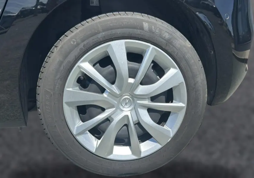 Gros plan sur la roue avant droite d’une Opel Corsa noire, avec enjoliveur argenté et logo Opel au centre.