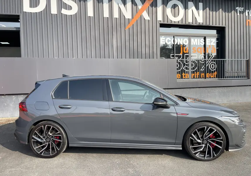 Profil côté gauche d'une Volkswagen Golf VIII GTI gris métallisé avec jantes noires à détails argentés et étriers rouges.