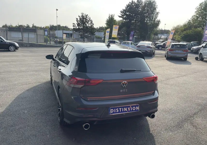Vue 3/4 arrière d'une Volkswagen Golf VIII GTI gris métallisé avec double sortie d'échappement et vitres teintées.
