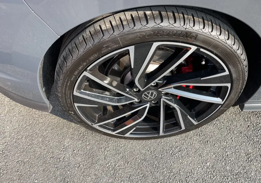 Gros plan sur la roue avant droite grise d'une Volkswagen Golf VIII GTI avec jante noire et détails rouges du frein.