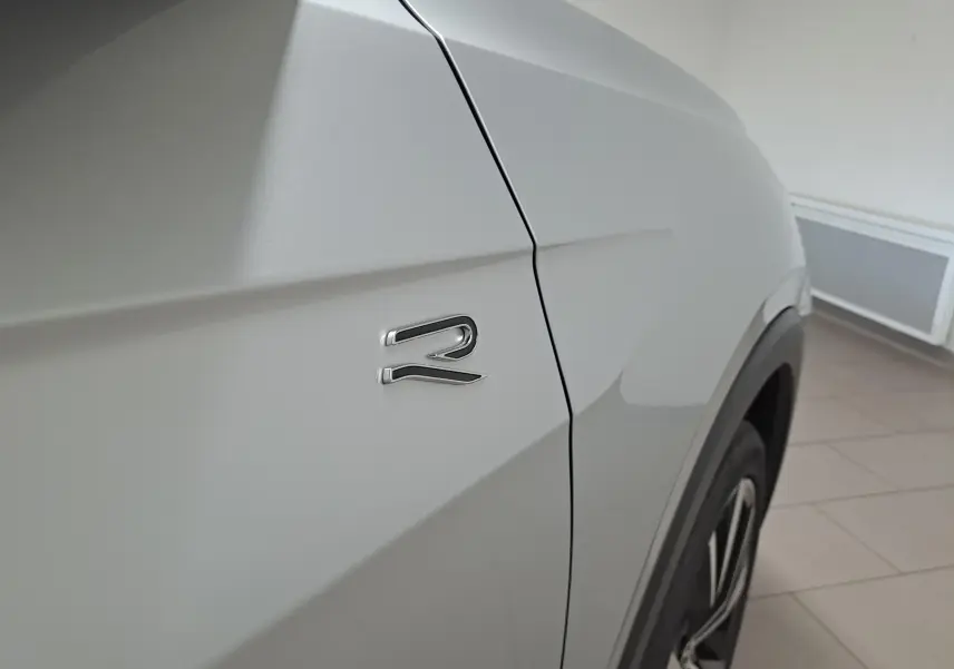 Gros plan sur l'aile avant droite argentée du Volkswagen T-Cross 2025 avec logo R et jante alliage visible.