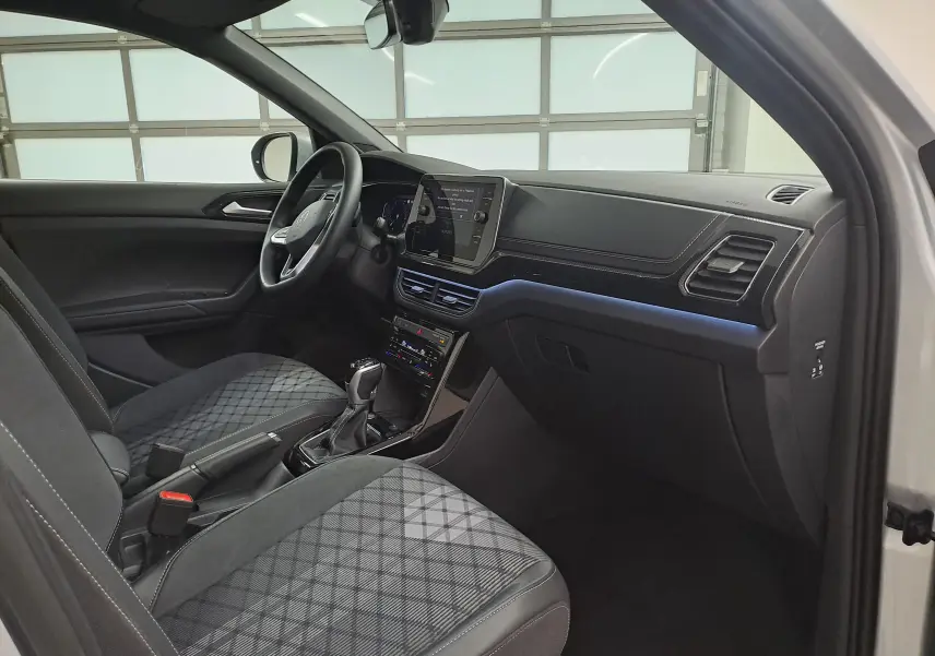 Intérieur côté conducteur du Volkswagen T-Cross 2025 argent, sièges avant chauffants avec motif quadrillé et tableau de bord moderne.
