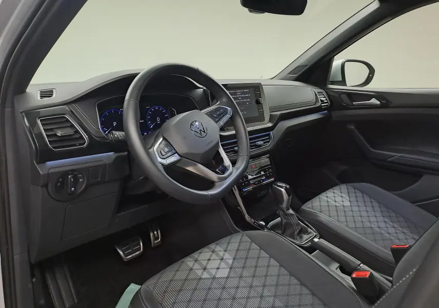 Intérieur du Volkswagen T-Cross 2025, vue côté conducteur, sièges tissu à motif, volant multifonction et console centrale moderne.