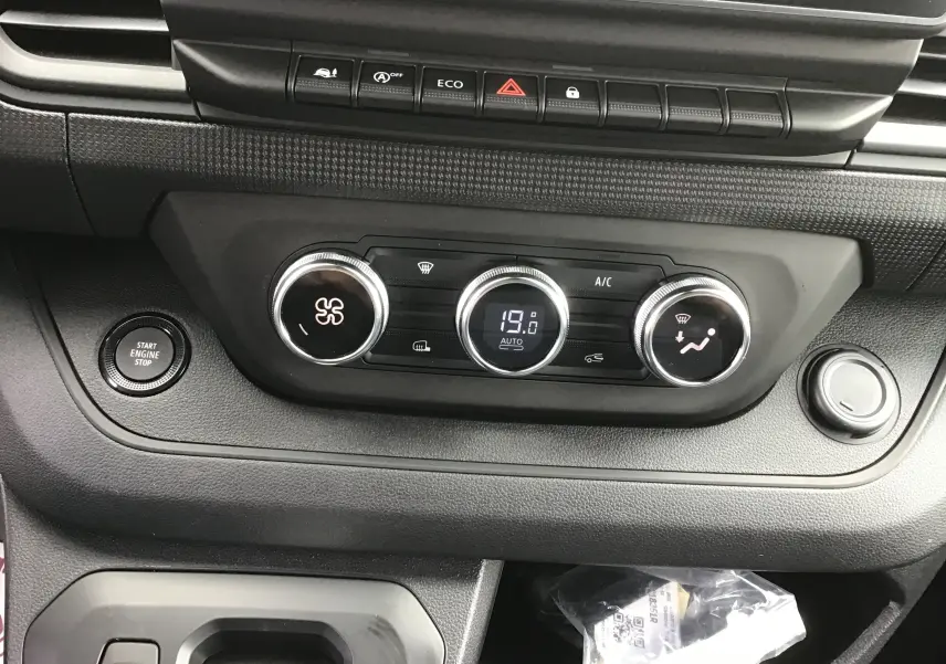 Détail du tableau de bord du Renault Trafic Fourgon gris comète, montrant les commandes de climatisation et le bouton Start/Stop.