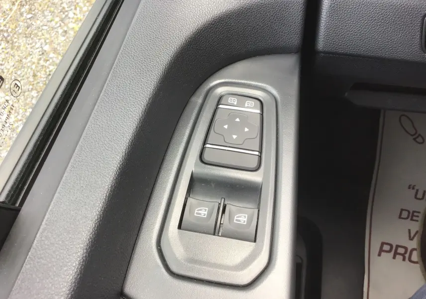 Gros plan sur les commandes électriques des vitres et rétroviseurs côté conducteur du Renault Trafic Fourgon gris Comète 2025.