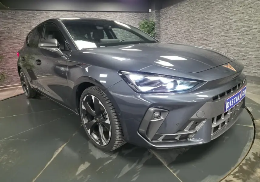 Vue 3/4 avant d'une CUPRA Leon gris magnétique avec phares Tri-LED allumés et jantes alliage 18 pouces.