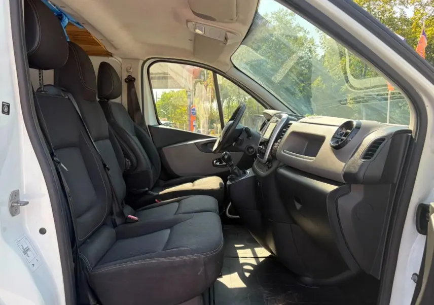 Vue intérieure côté conducteur du Renault Trafic Fourgon blanc 2018, montrant les sièges noirs et le tableau de bord.