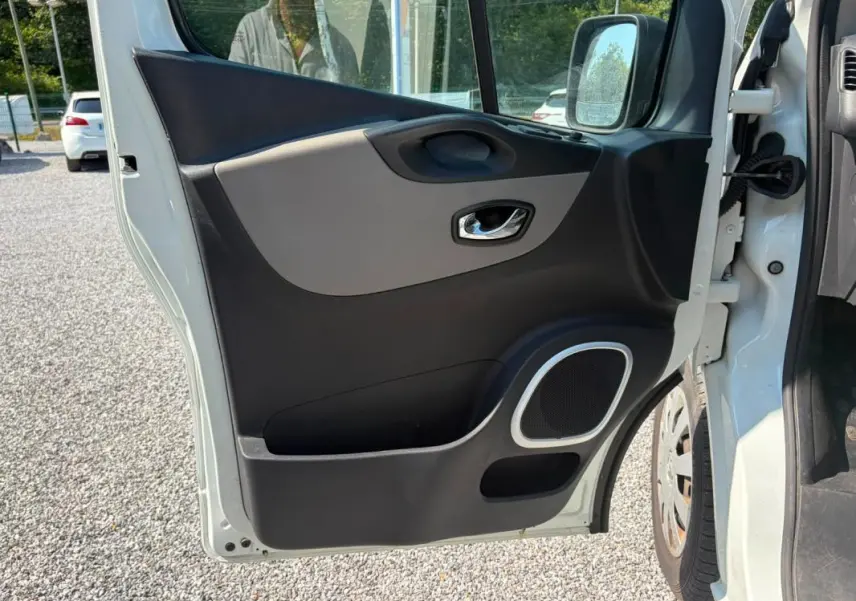 Vue rapprochée de la porte avant droite ouverte du Renault Trafic Fourgon blanc, montrant la garniture intérieure noire et grise avec haut-parleur intégré.