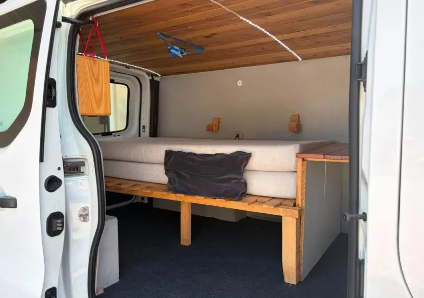 Vue intérieure côté droit du Renault Trafic Fourgon blanc 2018, montrant un aménagement avec lit et plafond en bois.