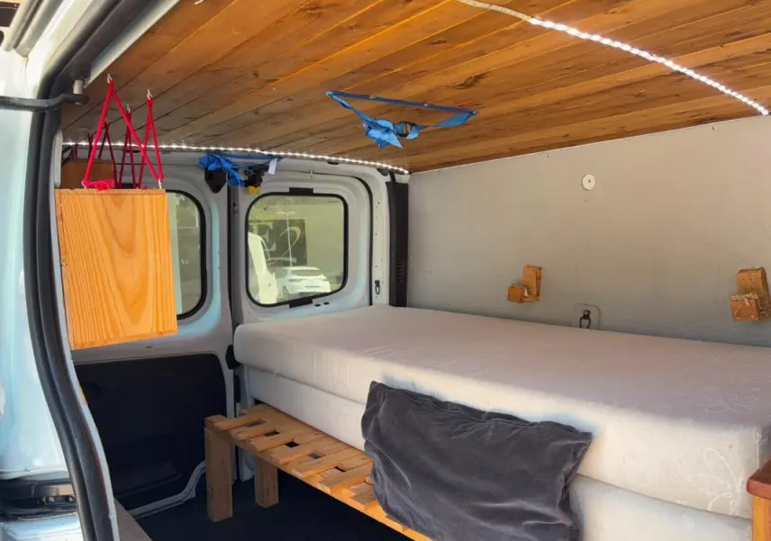 Intérieur du Renault Trafic Fourgon blanc vu de l'arrière, aménagé avec un lit, plafond en bois et éclairage LED.