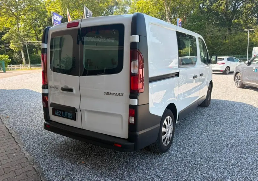 Vue 3/4 arrière droite d’un Renault Trafic Fourgon blanc de 2018 avec vitres arrière teintées et logo visible.