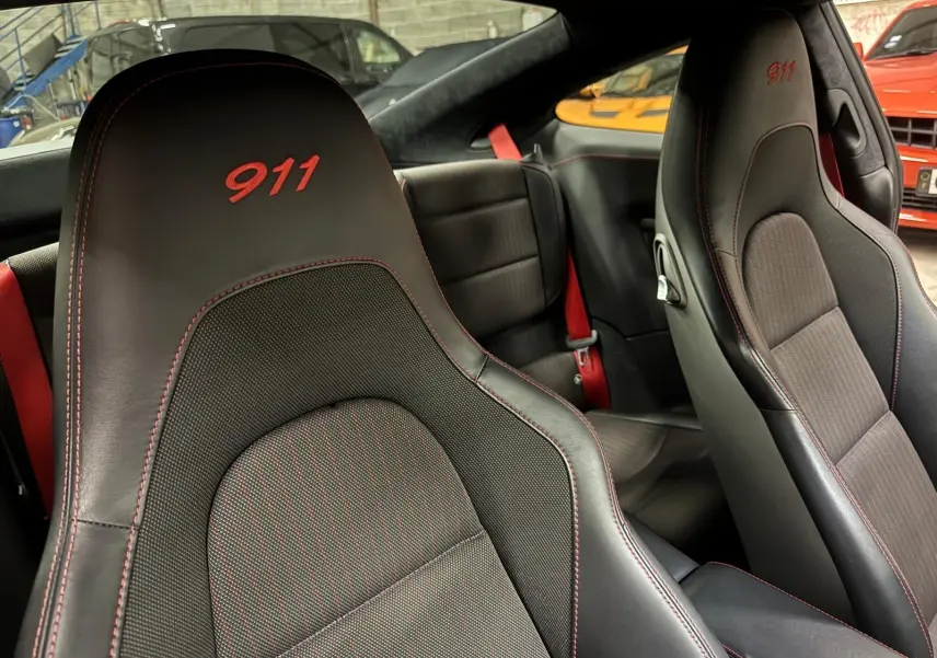 Gros plan sur les sièges avant noirs avec surpiqûres rouges et broderie "911" dans l'habitacle d'une Porsche 911 991.2.