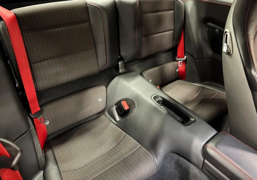 Vue rapprochée de l'arrière intérieur d'une Porsche 911 991 2 Carrera T avec sièges noirs et surpiqûres rouges, ceintures rouges visibles.