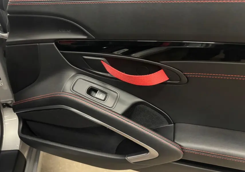 Gros plan sur la porte intérieure gauche noire avec surpiqûres rouges et poignée de maintien rouge du Porsche 911 991.2 Carrera T.