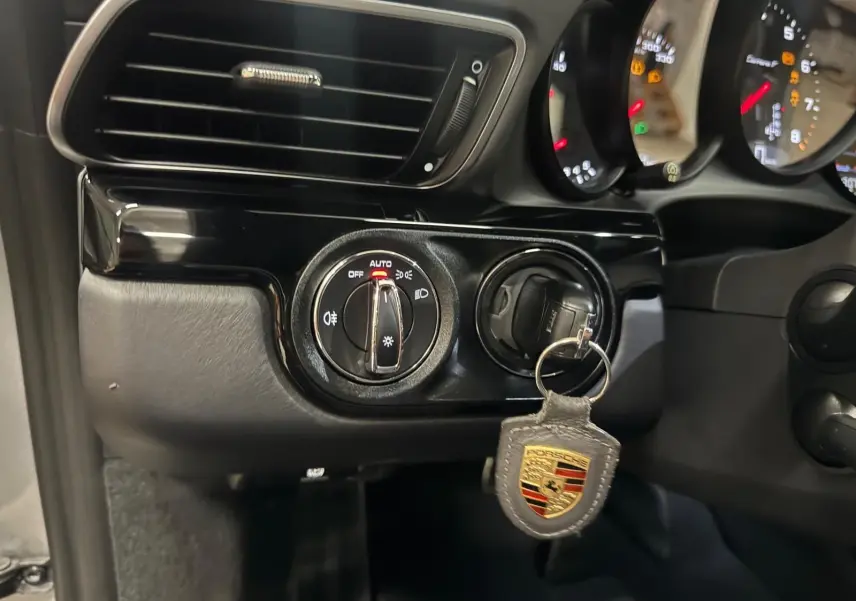 Gros plan sur le contacteur d’éclairage et la clé Porsche avec porte-clés dans l’habitacle noir d’une 911 991 Gris GT Silver.