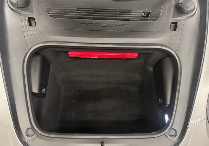 Vue plongeante sur le coffre avant ouvert d'une Porsche 911 991 2 Carrera T gris GT Silver, avec logo Porsche visible.