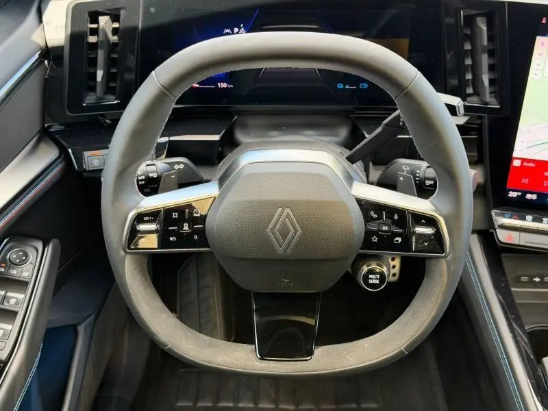 Vue rapprochée du volant multifonction noir avec logo Renault, tableau de bord digital et écran tactile latéral.