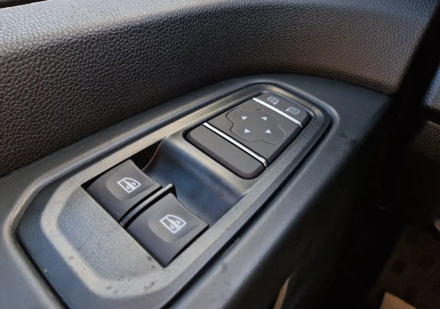 Gros plan sur les commandes de lève-vitres et réglage des rétroviseurs côté gauche du Renault Trafic Fourgon gris Highland.