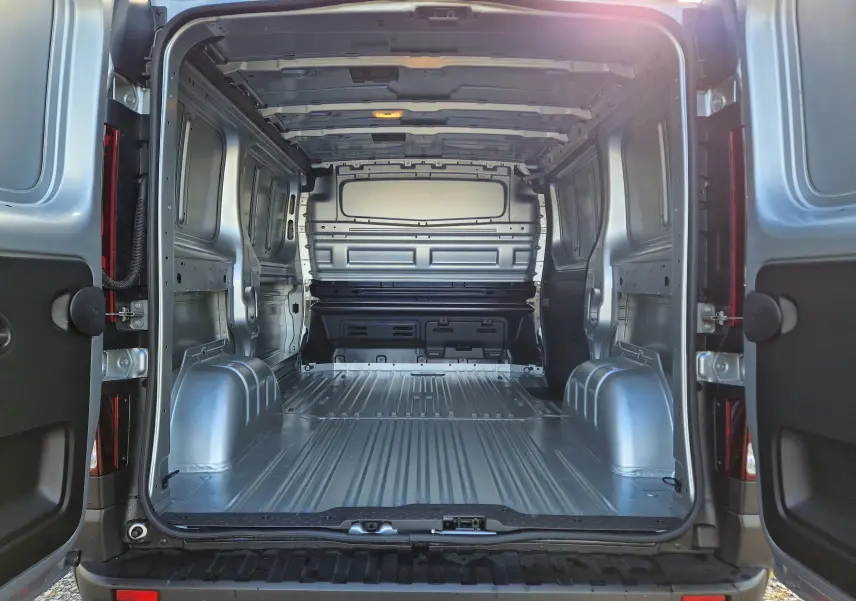 Vue arrière ouverte du Renault Trafic Fourgon gris Highland 2025, montrant l’espace de chargement métallique vide.