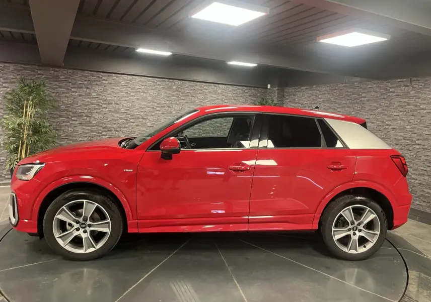 Audi Q2 S line rouge vue de profil côté gauche, toit et montant arrière blancs contrastants, jantes sport 5 branches.