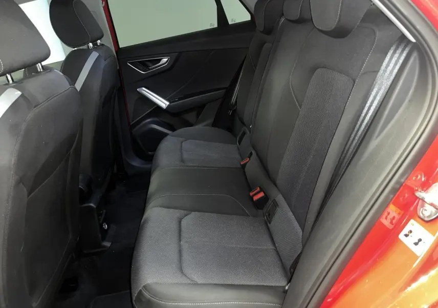 Vue intérieure côté arrière droit d’un Audi Q2 rouge 2024, montrant la banquette arrière en tissu noir avec ceinture de sécurité grise.