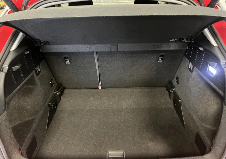 Vue intérieure du coffre ouvert de l'Audi Q2 rouge 2024, montrant un espace de rangement propre et bien éclairé.