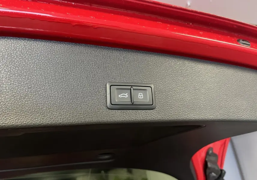 Bouton d'ouverture et de verrouillage du hayon électrique sur la face intérieure du coffre rouge d'un Audi Q2 S line.