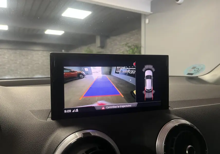 Écran central montrant la caméra de recul et l’aide au stationnement dans un Audi Q2 rouge stationné en intérieur.