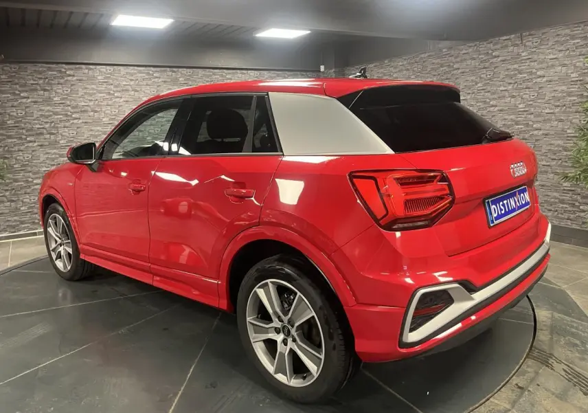 Audi Q2 rouge S line vue 3/4 arrière droit avec toit et montant arrière contrastés gris clair en intérieur showroom.
