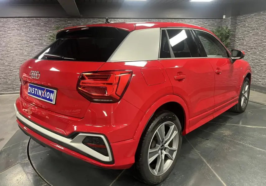 Audi Q2 rouge S line vue 3/4 arrière droit avec toit contrasté blanc et jantes sport 5 branches.