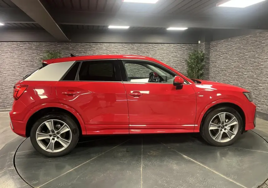 Audi Q2 rouge vue de profil côté gauche, avec toit contrasté blanc et jantes sport 5 branches.