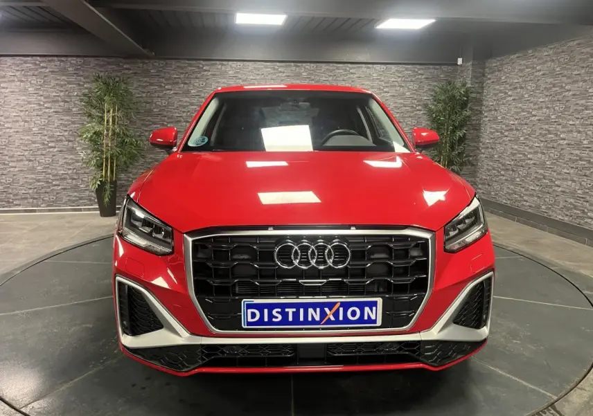 Vue frontale d'un Audi Q2 rouge 2024 avec calandre noire et détails argentés dans un showroom.
