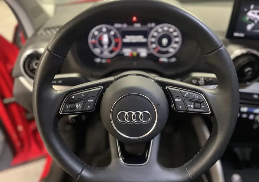 Volant sport en cuir noir avec méplat et commandes multifonctions dans l'Audi Q2 rouge 2024, vue de face intérieure.