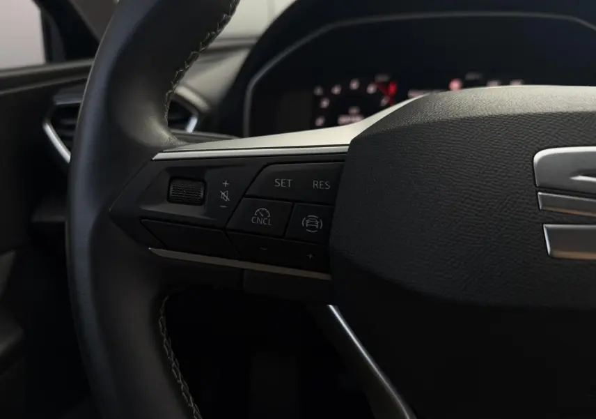Gros plan sur le volant cuir multifonction de la SEAT LEON ST 1.5 TSI, avec commandes de régulateur et logo SEAT visible.